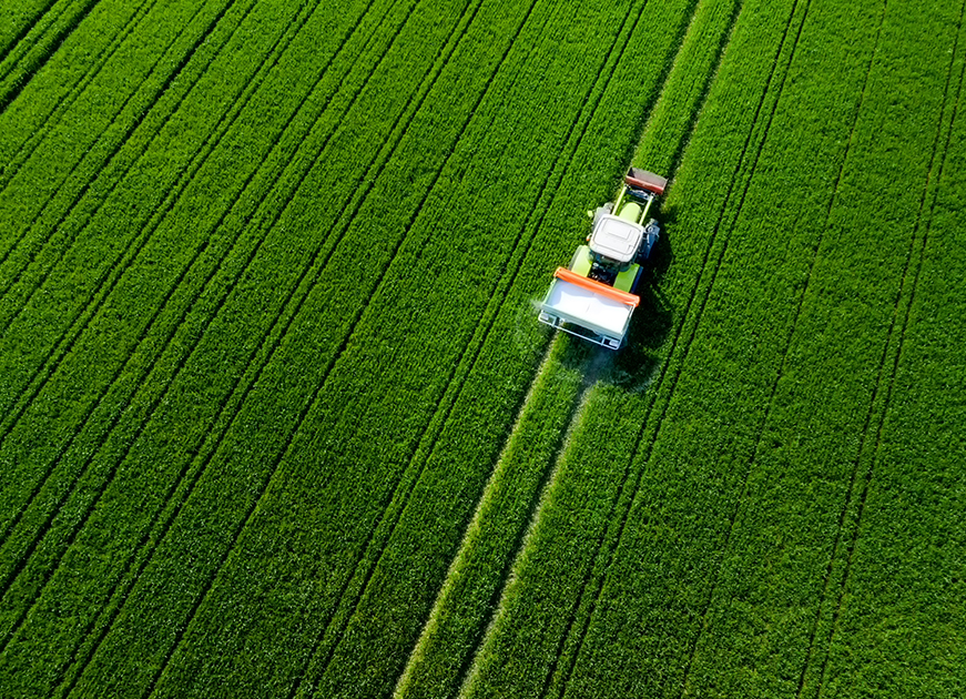 Ammoniumsulfat als Düngemittel - Traktor fährt über ein grünes Feld